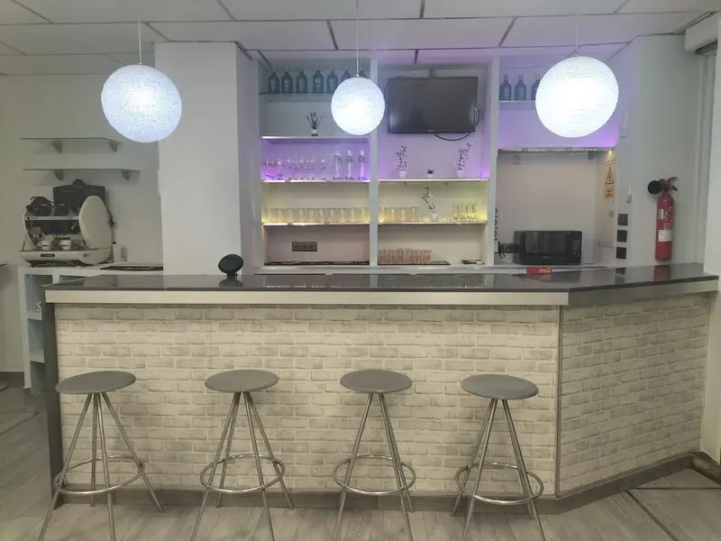 Barra de bar profesional con taburetes y estantería retroiluminada en local de eventos